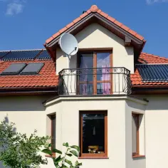Elegancki wykusz w domu z balkonem i oknami, na dachu panele słoneczne i antenę satelitarną.