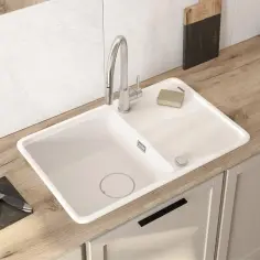 Nowoczesny biały zlew z baterią, obok deska do krojenia z ziołami. Zastanawiasz się, ile kosztuje montaż baterii zlewozmywakowej?