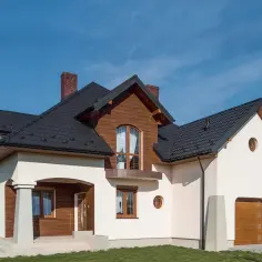 Elegancki dom z drewnianymi elementami i białym tynkiem. Solidny cokół na elewacji chroni budynek.