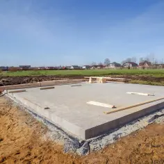 Płyta fundamentowa, jeden z rodzajów fundamentów, gotowa pod budowę domu. W tle domy i błękitne niebo.