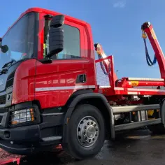 Czerwony hakowiec Scania gotowy do akcji. Sprawdź nasz wywóz gruzu cennik i pozbądź się odpadów budowlanych.