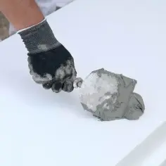 Ręka w rękawicy nakłada klej do styropianu na białą płytę. Zastanawiasz się, ile kleju do styropianu na m2 potrzebujesz do ocieplenia?