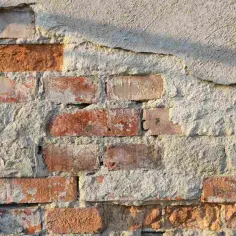 Fragment starego muru z cegły z odpadającym tynkiem.