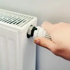 Dłoń reguluje termostat grzejnika, przygotowując dom na nadchodzący sezon grzewczy.