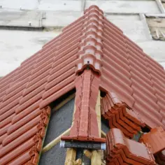 Nowy dach z brązowej dachówki, widoczne miejsce przecięcia dwóch połaci dachowych i stosy dachówek czekających na ułożenie.