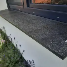 Montaż parapetów zewnętrznych po ociepleniu. Elegancki, ciemny parapet z granitu pięknie komponuje się z białym tynkiem i kwitnącą lawendą.