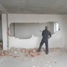 Mężczyzna z młotem burzy ścianę nośną. Gruz i cegły leżą na podłodze.