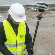 Geodeta w kamizelce odblaskowej i kasku z instrumentem Leica na budowie.