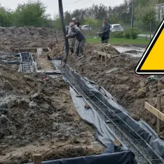 Budowa trwa! Wylewanie betonu na zbrojenie fundamentów. Widać koparkę i pracowników.