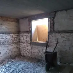 Wnętrze w remoncie, odsłonięte kamienne i ceglane ściany. Widać gruz i taczkę, zastanawiamy się, co zamiast tynku wewnątrz.