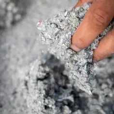 Dłoń trzymająca szarą, włóknistą masę. To celuloza, materiał izolacyjny z recyklingu.