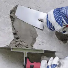 Ręce w rękawicach nakładają zaprawę na betonową posadzkę, wykonując naprawę.