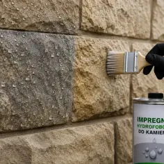 Rękawiczka i pędzel nanoszą impregnat hydrofobowy na kamienną ścianę, tworząc efekt perlenia wody.