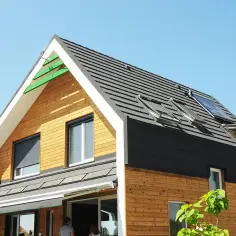 Nowoczesny dom energooszczędny z drewnianą elewacją, panelami słonecznymi i licznymi oknami dachowymi.