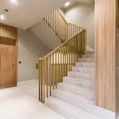 Nowoczesna klatka schodowa z drewnianymi elementami i złotymi balustradami. Zastanawiasz się, jaki tynk na klatce schodowej sprawdzi się najlepiej?