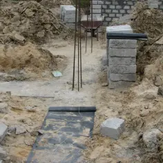 Budowa domu w toku. Widoczne wykopy, zbrojenie i materiały budowlane, tworzące fundamenty domu.