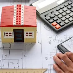 Model domu z klocków na planach, kalkulator i notatnik. Obliczanie, ile kosztuje wybudowanie domu 50m2.