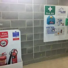 Tablica informacyjna budowy z gaśnicami, apteczką i instrukcjami.