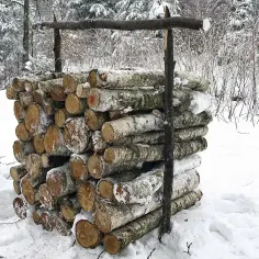 Zimowy stos drewna, prawdopodobnie metr sześcienny, przygotowany do palenia. Śnieg pokrywa pnie i otoczenie.