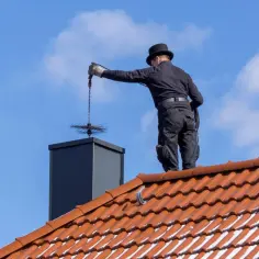 Kominiarz na dachu czyści komin. Zastanawiasz się, ile kosztuje przegląd kominiarski?