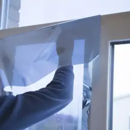 Nakładanie folii na okno, która przypomina efekt szkła weneckiego, nadając mu niebieskawy odcień.
