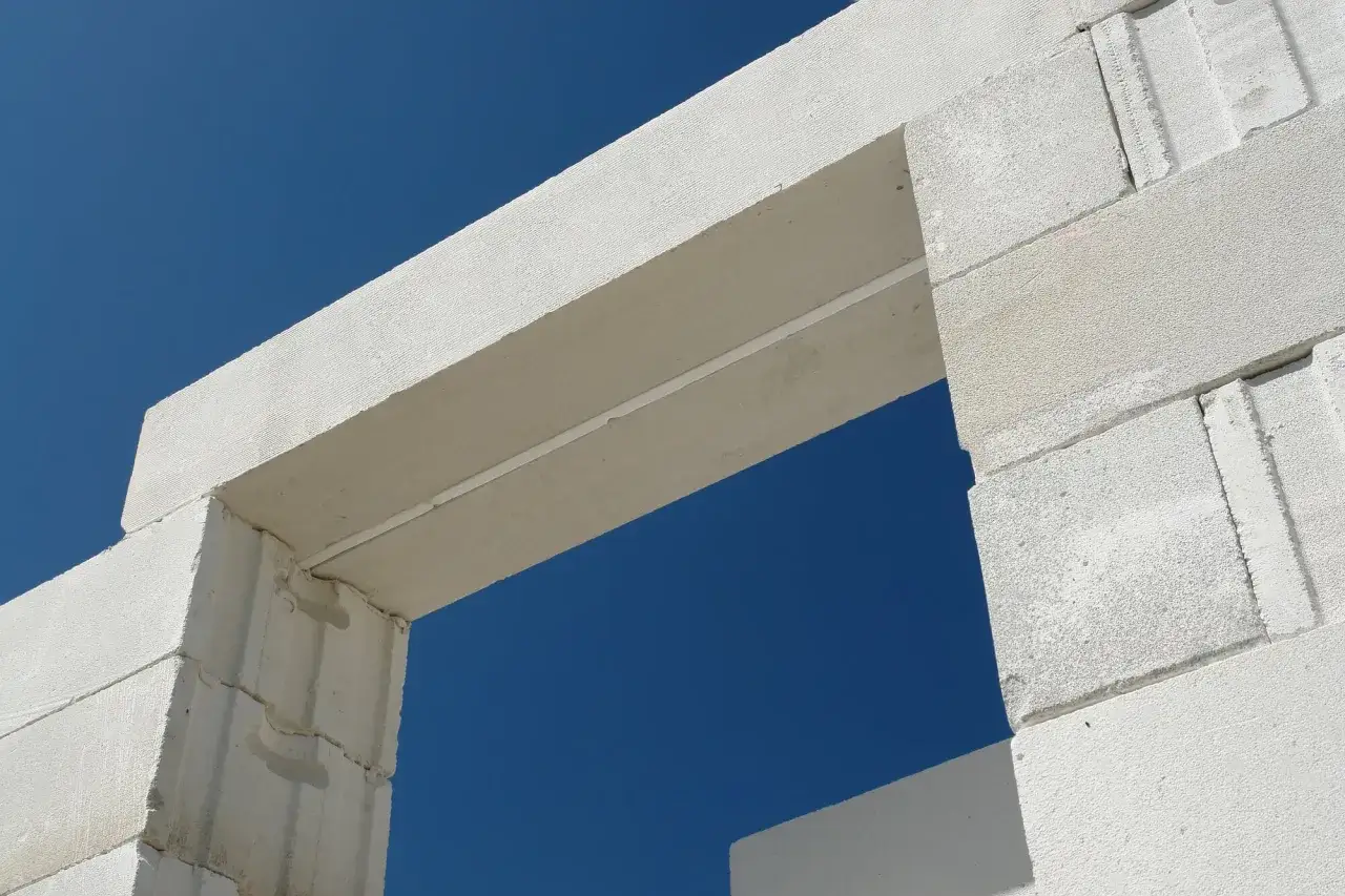 Biały nadproże z bloczków betonowych na tle błękitnego nieba. Konstrukcja czeka na dalsze prace budowlane.