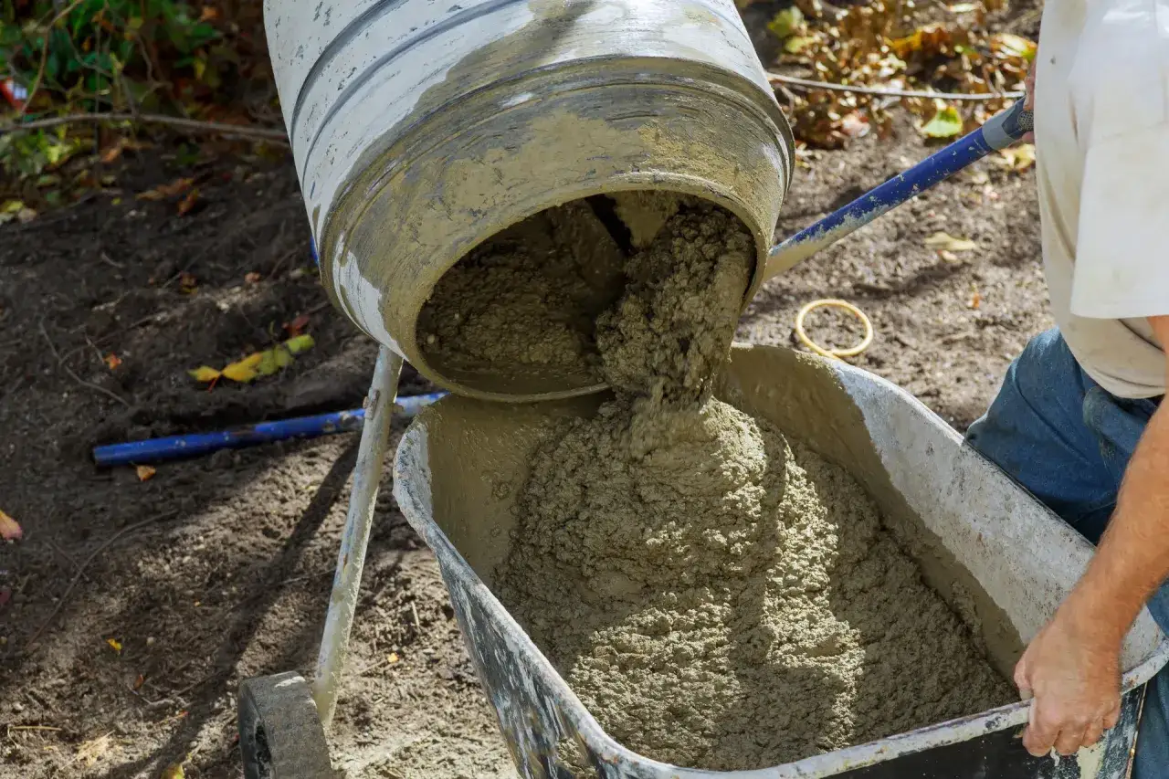Betoniarka wysypuje świeży beton do taczki. Nie ma znaczenia, ile łopat ma worek cementu, gdy liczy się efekt końcowy.