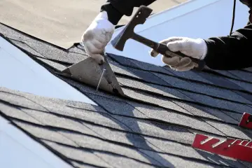 Ręce w rękawiczkach przybijają gonty. Widać fragmenty papy, która jest mocowana lepikiem do papy na zimno.