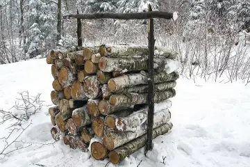 Zimowy stos drewna, prawdopodobnie metr sześcienny, przygotowany do palenia. Śnieg pokrywa pnie i otoczenie.