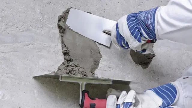 Ręce w rękawicach nakładają zaprawę na betonową posadzkę, wykonując naprawę.